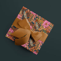 A wrapped gift with colorful floral garden party peony patterned paper and gold ribbon bow on dark background. Illustrated by Lisel Ashlock.