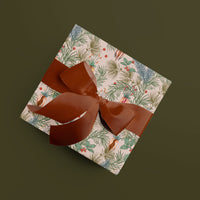 A wrapped gift with festive botanical wrapping paper featuring pine branches and red berries, tied with burgundy ribbon bows. Illustrated by Lisel Ashlock.