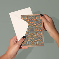 Hands holding an open apricot filigree thank you greeting card with decorative floral pattern. Illustrated by Lisel Ashlock.