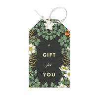 A dark green gift tag with botanical illustrations of white flowers, green leaves, and orange berries, featuring "a GIFT for YOU" text. Illustrated by Lisel Ashlock.