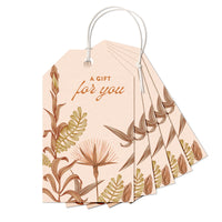A stack of cream gift tags with botanical illustrations in brown and gold featuring "A GIFT for you" text. Illustrated by Lisel Ashlock.