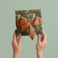 Two hands holding a wrapped gift with holly, berries, and hare pattern in moss tones with copper ribbon bow. Illustrated by Lisel Ashlock.