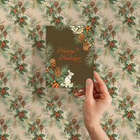 Hand holding holiday gift wrap featuring holly berries, pine cones, and hares on beige background. Illustrated by Lisel Ashlock.