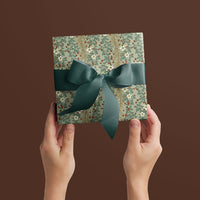 Two hands holding wrapped gift with sage floral pattern and teal ribbon bow against brown background. Illustrated by Lisel Ashlock.