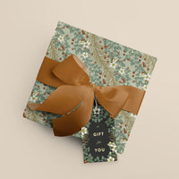 Rolled gift wrap with sage green botanical pattern and brown ribbon bow, labeled "A Gift for You." Illustrated by Lisel Ashlock.