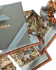 Linna California silk twill scarf with floral pattern, displayed with packaging and coordinating scrunchie. Illustrated by Lisel Ashlock.
