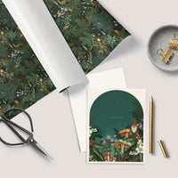 Flat lay of holiday greeting card with gnome and woodland scene, surrounded by coordinating wrapping paper and office supplies. Illustrated by Lisel Ashlock.