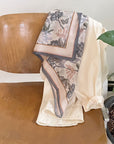 A silk cotton scarf with botanical and butterfly print draped over a wooden chair next to potted plants. Illustrated by Lisel Ashlock.