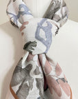 Silk cotton scarf in cream with blue, gray, and mauve botanical leaf patterns, gathered at center. Illustrated by Lisel Ashlock.
