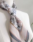 Angelite silk cotton scarf with botanical illustrations in soft gray, blush, and cream tones draped on a dress form. Illustrated by Lisel Ashlock.