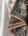 Folded silk cotton scarf in charcoal with botanical illustration in cream and copper tones. Illustrated by Lisel Ashlock.
