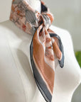 Sunstone silk cotton scarf draped on a white mannequin bust displaying botanical floral patterns in terracotta and gray tones. Illustrated by Lisel Ashlock.