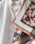 Silk cotton scarf with botanical floral pattern in coral and black tones draped over white shirt. Illustrated by Lisel Ashlock.