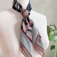 Silk cotton scarf in moonstone featuring botanical illustrations of pink flowers on dark navy background, styled on dress form. Illustrated by Lisel Ashlock.