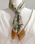 Silk cotton scarf with anemone floral pattern in green, cream, and gold tones, tied at neck. Illustrated by Lisel Ashlock.
