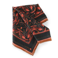 A folded silk cotton scarf in bright mahogany filigree pattern with floral motifs and brown border trim. Illustrated by Lisel Ashlock.