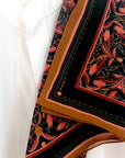 Folded silk cotton scarf in bright mahogany filigree pattern with red, gold, and black floral design. Illustrated by Lisel Ashlock.