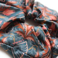 Close-up of a blue silk scrunchie with red and orange rose pattern, gathered and folded. Illustrated by Lisel Ashlock.