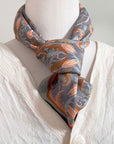 Apricot Filigree silk cotton scarf tied around a mannequin wearing a cream linen shirt. Illustrated by Lisel Ashlock.