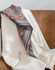 Silk cotton scarf with apricot filigree pattern draped over wooden chair. Illustrated by Lisel Ashlock.