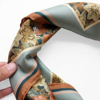 Hand holding folded silk twill scarf with botanical floral pattern in cream, rust, and teal. Illustrated by Lisel Ashlock.