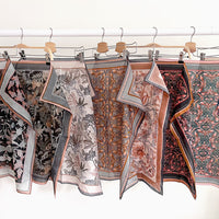 Collection of patterned silk cotton scarves in earth tones hung on wooden hangers. Illustrated by Lisel Ashlock.