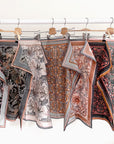 Collection of patterned silk cotton scarves in earth tones hung on wooden hangers. Illustrated by Lisel Ashlock.
