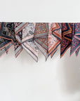 Multiple silk cotton scarves with floral and geometric patterns in apricot, navy, and blush tones displayed on a rod. Illustrated by Lisel Ashlock.