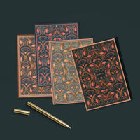 A collection of ornate thank you greeting cards with red and gold filigree floral patterns on dark backgrounds, displayed with a gold pen. Illustrated by Lisel Ashlock.