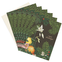 Stack of holiday greeting cards with dark green botanical design featuring citrus fruits and white flowers, illustrated by Lisel Ashlock.