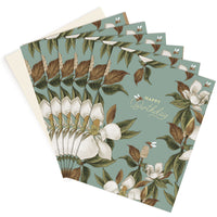 A stack of "Happy Birthday" greeting cards featuring white magnolia flowers, brown leaves, and honey bees on a sage green background. Illustrated by Lisel Ashlock.