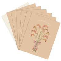 A stack of greeting cards with a beige background featuring pink and coral flowers tied with a pink ribbon and "celebrating you" text. Illustrated by Lisel Ashlock.