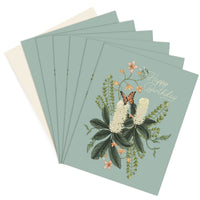 Stack of Happy Birthday greeting cards with sage green background, white flowers, green foliage, and butterfly illustration by Lisel Ashlock.