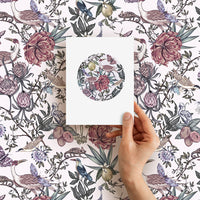 Hand holding a blank greeting card with circular floral design against patterned background. Illustrated by Lisel Ashlock.