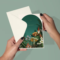 Hands holding an open greeting card with a whimsical garden gnome illustration and "Peace & Love" text. Illustrated by Lisel Ashlock.