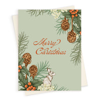Merry Christmas greeting card with holly, pinecones, berries, rabbit, and evergreen branches on sage green background. Illustrated by Lisel Ashlock.