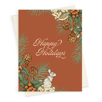 Holiday greeting card with rust background, illustrated pine cones, holly berries, white flowers, birds, and hare. Illustrated by Lisel Ashlock.