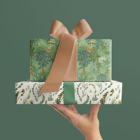 A hand holding stacked gift boxes wrapped in woodland-patterned paper with peach and green ribbons against a green background. Illustrated by Lisel Ashlock.