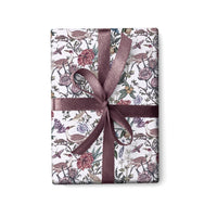 A wrapped gift with mauve ribbon featuring an illustrated pattern of birds, flowers, and botanical elements by Lisel Ashlock.