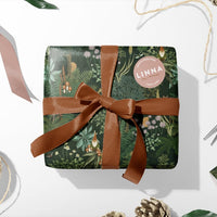 Green gift wrap with gnome and floral pattern tied with brown ribbon, surrounded by twine and decorative elements. Illustrated by Lisel Ashlock.