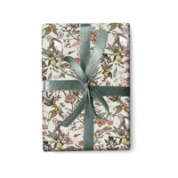 Gift wrap with botanical pattern featuring monkeys, flowers, and fruits tied with a sage green ribbon, illustrated by Lisel Ashlock.