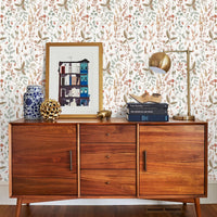 Mid-century wooden dresser styled with framed art, stacked books, brass lamp, and decorative objects against floral wallpaper. Illustrated by Lisel Ashlock.