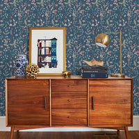 Mid-century modern wooden dresser against indigo floral wallpaper with framed art and gold lamp. Illustrated by Lisel Ashlock.