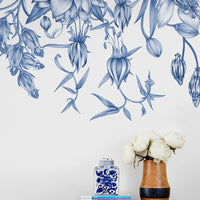 Blue and white botanical wall mural illustration above wooden shelf with books, blue porcelain jar, and white flowers in wooden vase. Illustrated by Lisel Ashlock.