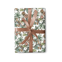 A roll of gift wrap featuring illustrated tropical birds and flowering plants tied with a rose gold ribbon, illustrated by Lisel Ashlock.