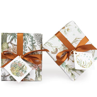 Two wrapped gift boxes with botanical illustrations, orange satin ribbons, and coordinating gift tags. Illustrated by Lisel Ashlock.