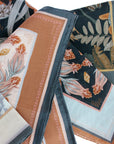 Folded silk cotton scarves in botanical prints featuring flowers and leaves in terracotta and teal. Illustrated by Lisel Ashlock.