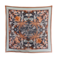 Square silk cotton scarf featuring symmetrical botanical and animal motifs in orange, gray, and black on pale blue border. Illustrated by Lisel Ashlock.