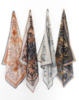 Four folded silk cotton scarves in earth tones featuring botanical and animal motifs. Illustrated by Lisel Ashlock.