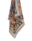 Silk cotton scarf in moonstone with botanical and animal motifs featuring monkeys, ferns, and flowers in black, orange, and cream. Illustrated by Lisel Ashlock.